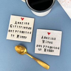 A square white coaster with a heart at the top with black text: Amazing Wives get promoted to Mummy
A square white coaster with a heart at the top with black text: Amazing Girlfriends get promoted to Mummy