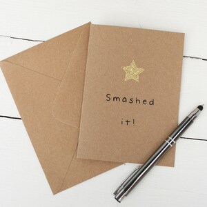 May include: A brown card with a gold glitter star and the text "Smashed it!"  The card is sitting on a brown envelope.