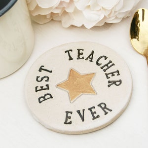 White round coaster with gold star in the centre and black text around the edge: BEST TEACHER EVER