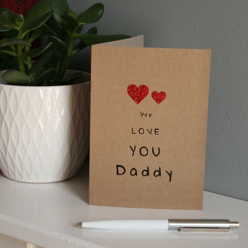 kraft card with black text we love you daddy with 1 big and 1 small red glitter hearts