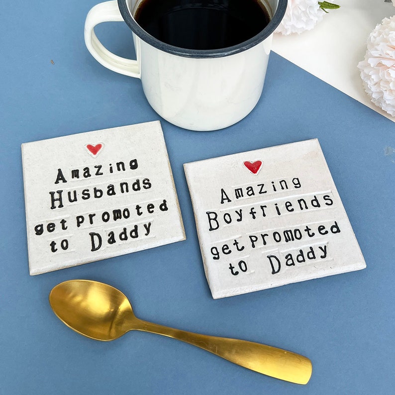 A square white coaster with a heart at the top with black text: Amazing Husbands get promoted to Daddy
A square white coaster with a heart at the top with black text: Amazing Boyfriends get promoted to Daddy