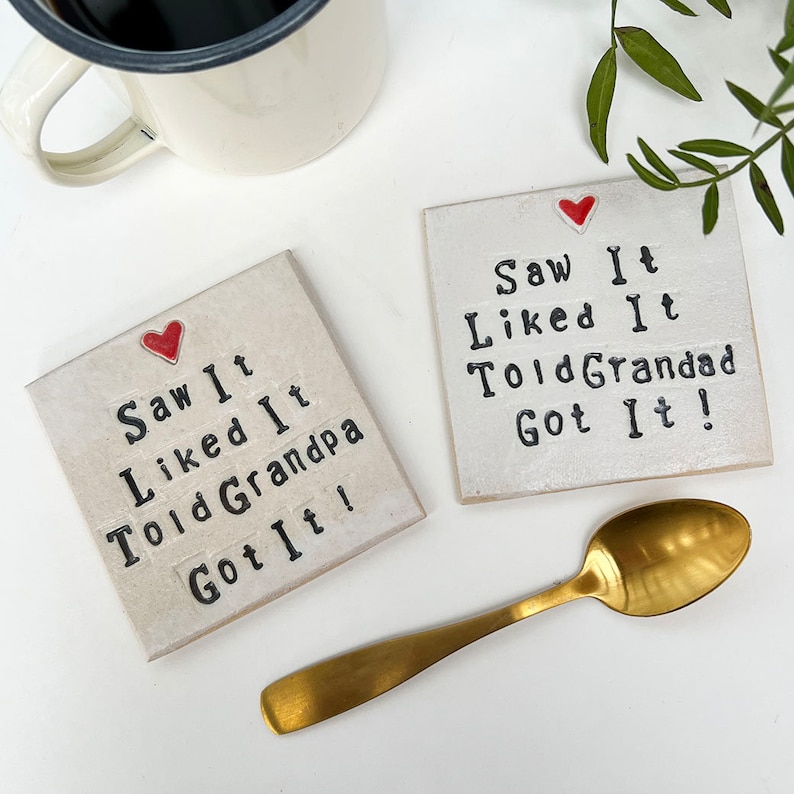 K&ouml;nnte beinhalten: Zwei wei&szlig;e Keramik-Untersetzer mit schwarzem Text und einem roten Herzen. Der Text auf den Untersetzern lautet "Saw It Liked It Told Grandpa Got It!" und "Saw It Liked It Told Grandad Got It!"