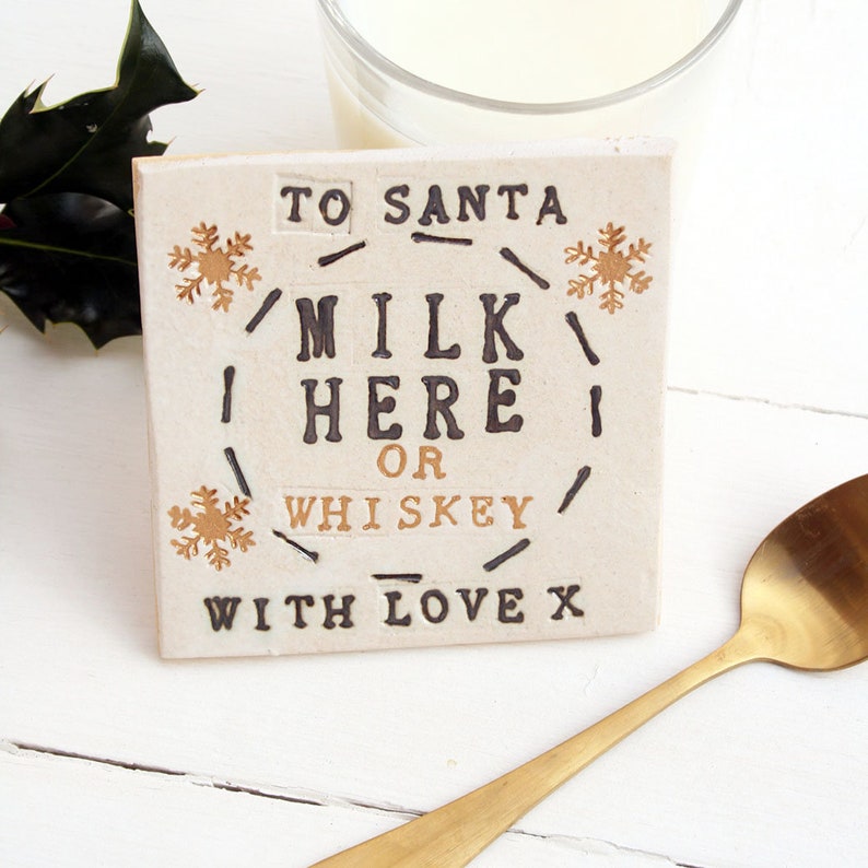 Square white coaster with gold snowflakes and black text: MILK HERE or whiskey, with love x