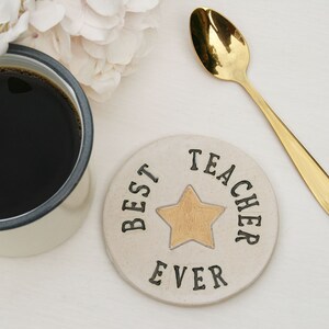 White round coaster with gold star in the centre and black text around the edge: BEST TEACHER EVER