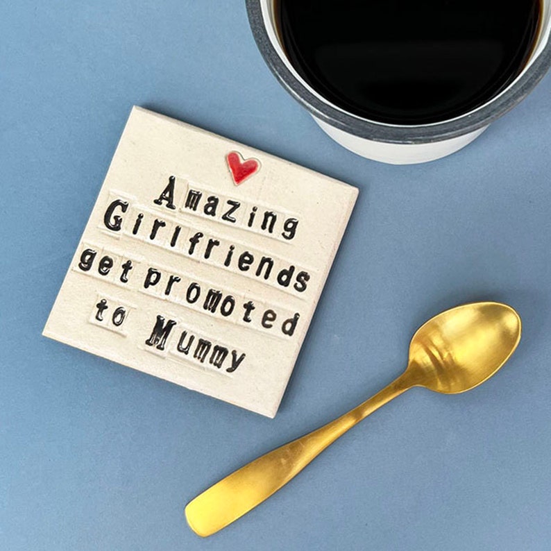 A square white coaster with a heart at the top with black text: Amazing Girlfriends get promoted to Mummy