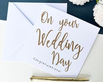 May include: A white card with gold lettering that says "On your Wedding Day Congratulations!"
