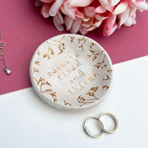 Approx 9cm round white glaze dish. Text: nanna's rings and things. Written in gold, as are the flowers imprinted around the edge of the dish.