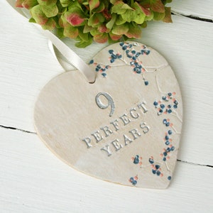 May include: White ceramic heart-shaped ornament with a silver number 9 and the text "PERFECT YEARS" in silver lettering. The ornament is decorated with a floral design in blue and pink.