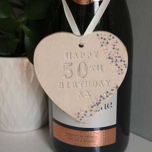 white ceramic hanging heart with pretty pink and blue flowers along the right hand side and silver text: Happy 50th birthday xx. finished with cream satin ribbon