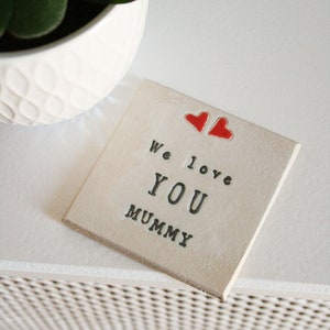 white square coaster with two hearts at the top with the same black text: We love you mummy
