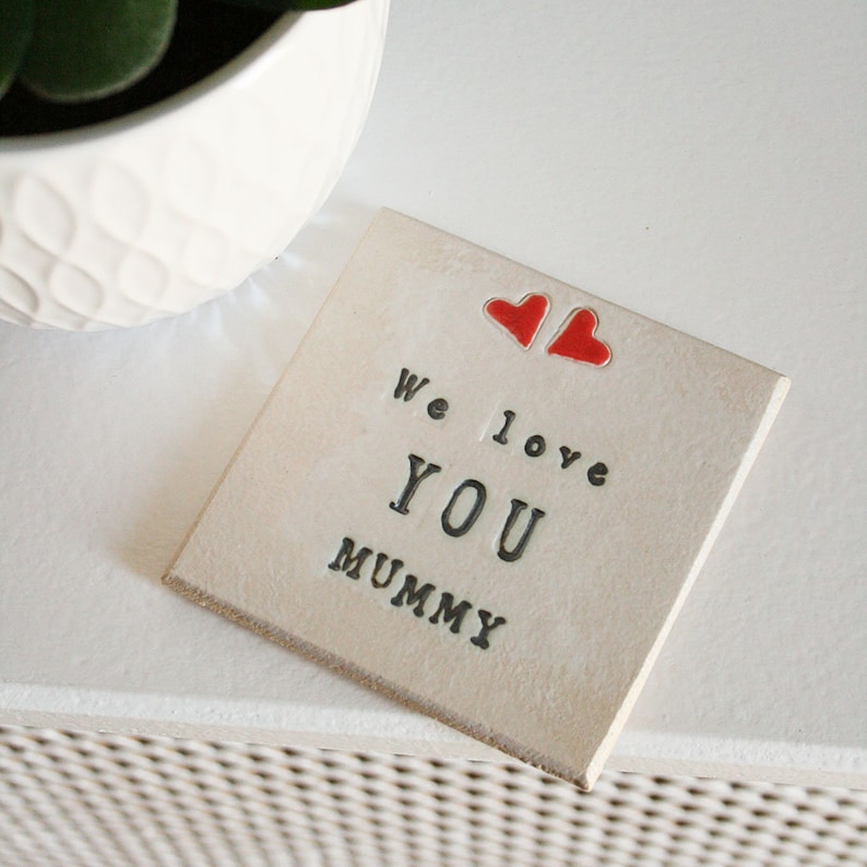 white square coaster with two hearts at the top with the same black text: We love you mummy