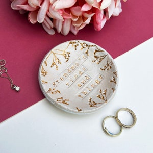 Approx 9cm round white glaze dish. Text: grandma's rings and things. Written in gold, as are the flowers imprinted around the edge of the dish.