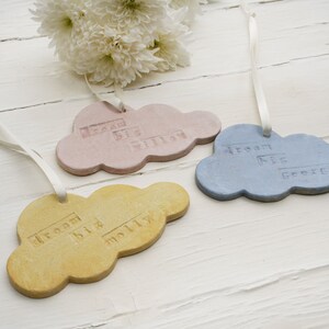 May include: Three pastel-coloured ceramic cloud ornaments with white ribbon hangers. Each cloud has the text "Dream Big" and a name: "William", "George", and "Molly".