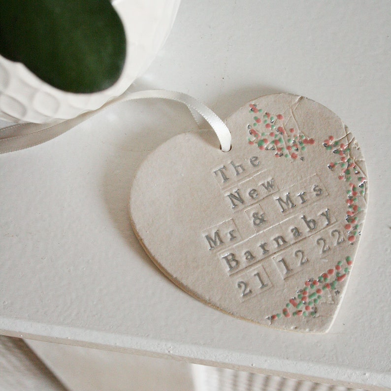 White hanging heart of cream ribbon, Pink and green flowers along the side with silver text: The New Mr & Mrs NAME DATE