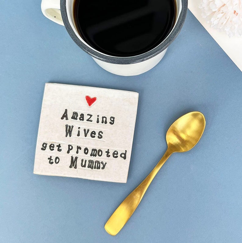 A square white coaster with a heart at the top with black text: Amazing Wives get promoted to Mummy
