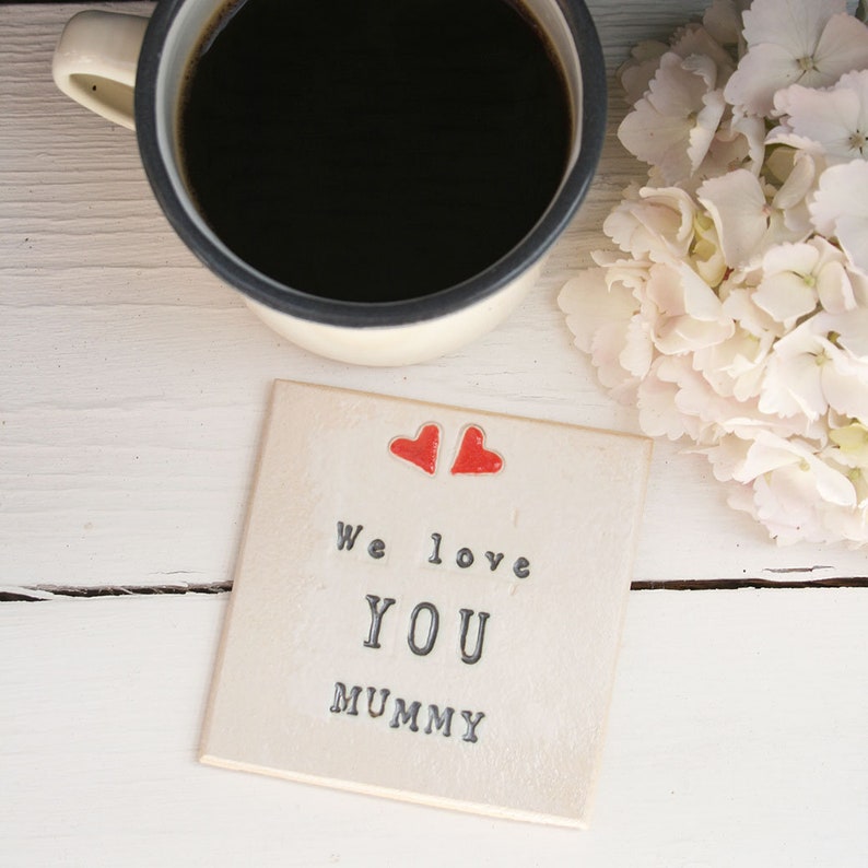 white square coaster with two hearts at the top with the same black text: We love you mummy