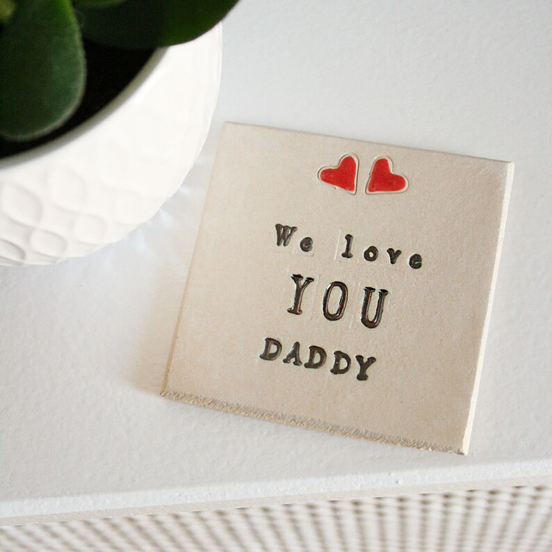 white square coaster with two hearts at the top with the same black text: We love you daddy