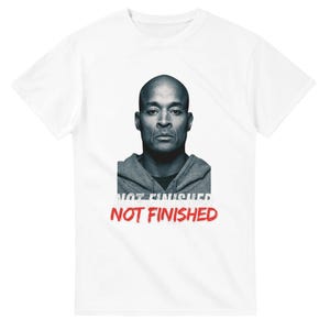 Può includere: Una t-shirt bianca a maniche corte con una grafica centrale raffigurante un uomo calvo che indossa una felpa grigia con cappuccio. Sotto il ritratto, il testo "NOT FINISHED" è stampato in un carattere rosso audace e usurato, con un leggero effetto ombra bianco.