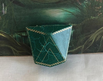 May include: A dark green, textured, geometric-shaped jewelry box with a triangular lid. The exterior features a subtle, cracked leather-like pattern and is accented with thin, gold-colored decorative lines along the edges and top surfaces.