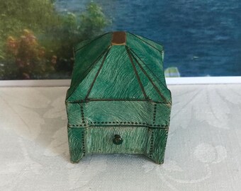 May include: A small, square-shaped box with a textured green finish and a peaked lid. The box features dark metal trim along the edges and a single small, centered knob on the front panel. The surface has a fine, brush-stroke pattern throughout.