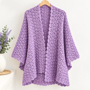 May include: A light purple crochet cardigan featuring an open-front design with a scalloped edge trim. The garment is crafted with a textured, lacy stitch pattern throughout, including the wide sleeves and the hemline, creating a lightweight layer.