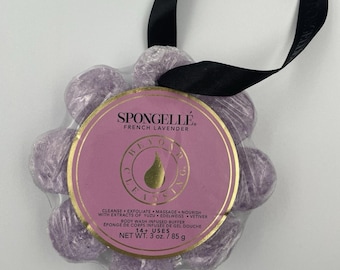 May include: A flower-shaped Spongellé body wash infused buffer in French Lavender. The purple sponge is wrapped in clear plastic with a round pink label featuring gold text and a black ribbon loop. Net weight is 3 oz. / 85 g.