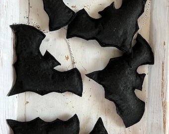 May include: A string of six black felt bats hanging from a white tray. The bats are all the same size and shape, and they are hanging in a staggered pattern.