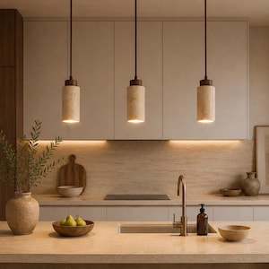 May include: Three cylindrical pendant lights with light beige stone shades and dark wood accents suspended from a horizontal dark wood ceiling mount. The lights hang above a kitchen island with a stone countertop and three wooden stools.