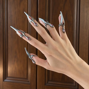 May include: A set of five silver-toned metal claw rings worn on the fingers. Each ring features a pointed, elongated tip, a cutout design, and a small, round, pink gemstone accent at the base near the finger joint.