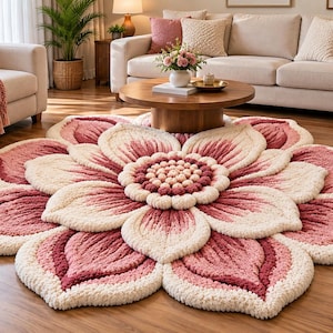 May include: A large, circular, tufted area rug shaped like a blooming flower. The rug features layered, petal-like sections in shades of cream, soft pink, and deep rose, with a textured, pom-pom style center in matching pink and cream tones.