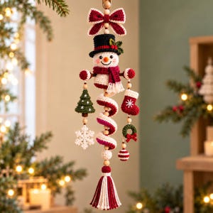 May include: A crocheted hanging ornament featuring a snowman wearing a black top hat and a maroon scarf. The snowman is attached to a spiral structure with dangling crocheted elements including a green tree, a white snowflake, a red stocking, a green wreath, and a red and white striped ball, finished with a maroon and white tassel.