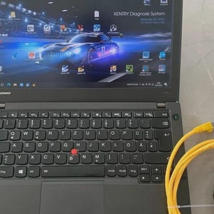 Könnte beinhalten: Ein schwarzer Lenovo ThinkPad Laptop mit QWERTZ-Tastatur und rotem Trackpoint, der einen Desktop-Hintergrund mit einem blauen Sportwagen und dem Text XENTRY Diagnosis System Release 06-2025 anzeigt. Ein gelbes Ethernet-Kabel liegt aufgerollt daneben.