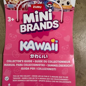 May include: A pink Zuru Mini Brands Kawaii collector's guide featuring illustrations of miniature food items, a rabbit character, and text including Mini Brands, Kawaii, and Collector's Guide. The guide has a handle shape at the top and a 3+ age rating.
