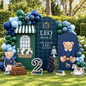 May include: A party backdrop display featuring green and blue balloons, a green structure with a window, a plaid panel with text reading LEO turns 2, and a blue panel with a teddy bear illustration. Includes a number 2 sign and vintage suitcases.