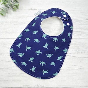 May include: A blue baby bib with a white trim and a pattern of green sea turtles.