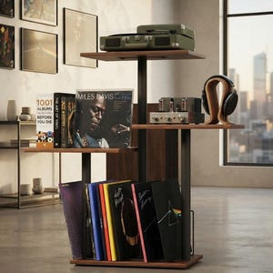 May include: A multi-tiered wooden record storage stand with black metal supports. The top shelf holds a green portable record player. The middle shelf features a vacuum tube amplifier and headphones on a stand. The bottom shelf displays vinyl records.