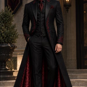 May include: A long black coat featuring red embroidery on the lapels and cuffs, worn over a black vest with a subtle pattern, a black shirt, a dark red tie, and black trousers. The coat has a deep red patterned lining visible at the bottom.
