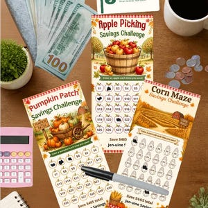 May include: Three paper savings challenge trackers featuring Apple Picking, Pumpkin Patch, and Corn Maze themes. Each tracker includes illustrations, currency-denominated icons to colour, and the text Jen-uine Savings. Includes a black marker and cash.