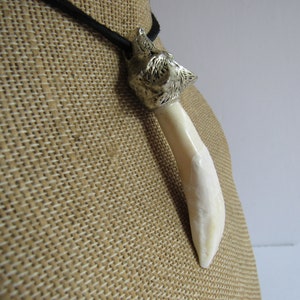 May include: A silver wolf head pendant with a white tooth-shaped charm hanging from a black cord.