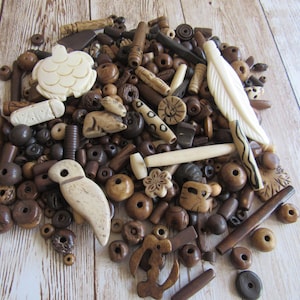 May include: A collection of wooden beads and decorative elements in various shapes and sizes. The assortment includes beads, carved birds, a turtle, a feather, and other unique designs in shades of brown and cream.