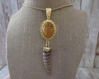 May include: A gold-toned pendant necklace featuring an oval amber-colored stone in a filigree setting. A spiral-shaped pendant hangs below. The necklace is displayed on a burlap-covered bust.
