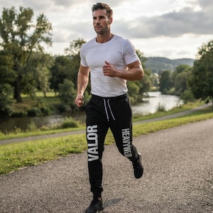 Könnte beinhalten: Ein schlichtes weißes Kurzarm-T-Shirt mit Rundhalsausschnitt kombiniert mit einer schwarzen Jogginghose mit weißen Kordelzügen und dem vertikal aufgedruckten weißen Schriftzug VALOR HEAVYWEAR auf den Beinen, dazu schwarze Sportschuhe.