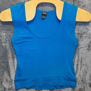 May include: A bright blue sleeveless tank top with a scoop neckline and a wide hem band. The garment features a black interior neck label with the white text dots. and the size XL printed below it, indicating the brand and size of the shirt.