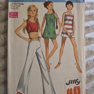 Può includere: Una busta per cartamodello vintage Simplicity 8214 per taglia junior petite 13JP con un busto di 89 cm. La copertina presenta illustrazioni di tre outfit: un top corto rosso con pantaloni bianchi, una tunica floreale verde con pantaloncini e un miniabito a righe.
