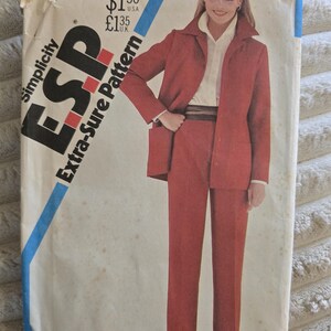 Pode incluir: Um envelope de molde de costura Simplicity ESP Extra-Sure Pattern 5697 com uma fotografia de um blazer e calças a condizer na cor ferrugem sobre uma camisa branca com colarinho. O envelope inclui texto indicando o tamanho K, 8, 10 e 12.