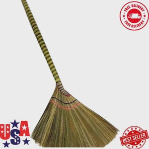 May include: A long-handled broom featuring a natural fibre bristle head that fans out in a wide triangular shape. The handle is wrapped in a yellow and black striped pattern, while the bristles are secured with thin red and black horizontal thread accents.