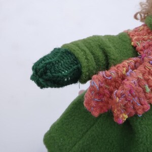 Op de afbeelding: Een groene gebreide want met een groene fleecejasmouw. De want heeft een wit stikseldetail.