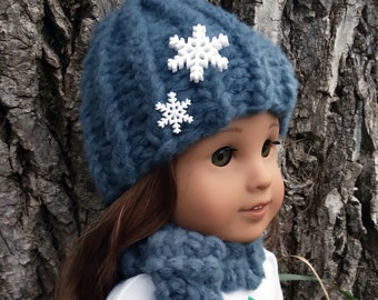 Puede incluir: Una muñeca con un gorro azul tejido con adornos de copo de nieve blanco, una bufanda azul tejida y una camisa blanca con un diseño de árbol de Navidad verde.