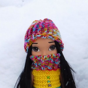 May include: Two dolls wearing colorful crocheted dresses and matching hats. The dresses are layered with rainbow stripes and the hats are multi-colored.