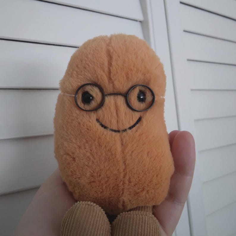Puede incluir: Un juguete de peluche con forma de jud&iacute;a, en tonos naranja y marr&oacute;n. El juguete tiene unas gafas peque&ntilde;as y redondas con montura de alambre y una sonrisa cosida. Los pies son de pana. El juguete est&aacute; dise&ntilde;ado para ser sujetado.